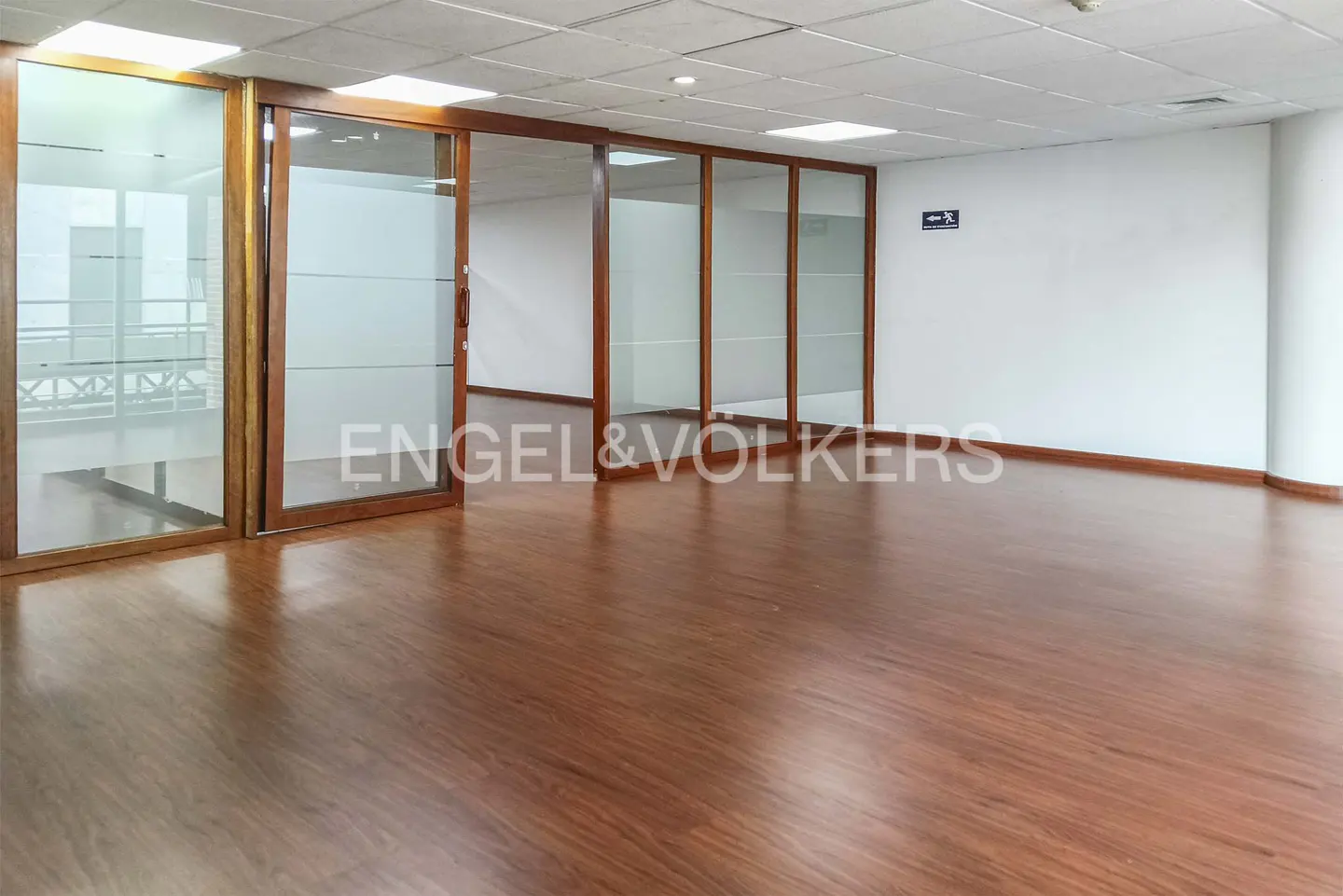 Empty office space with wood-look flooring, white walls, and glass partitions framed in wood.