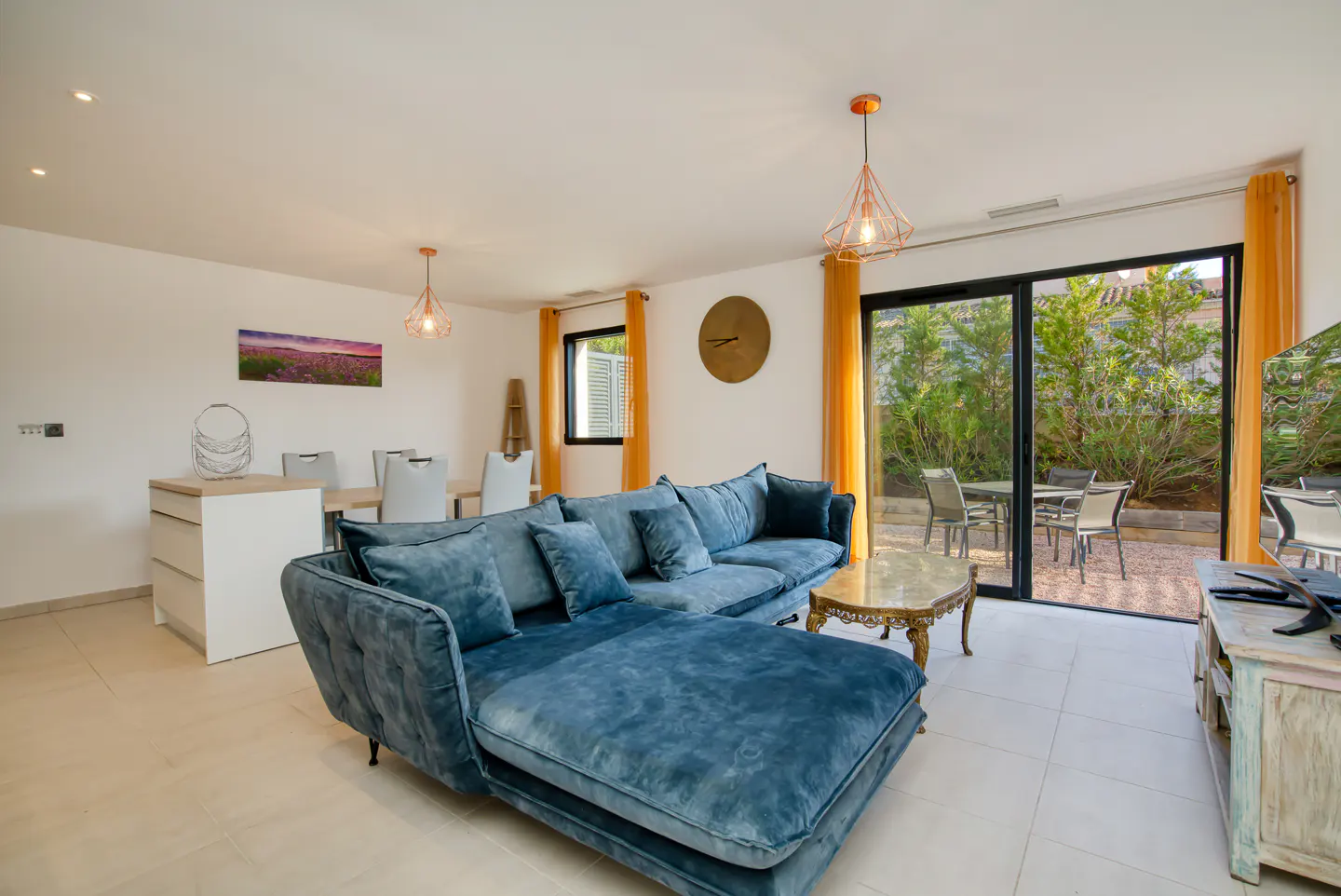 Bright living room with a blue velvet sectional sofa, marble coffee table, and sliding glass doors to a patio.