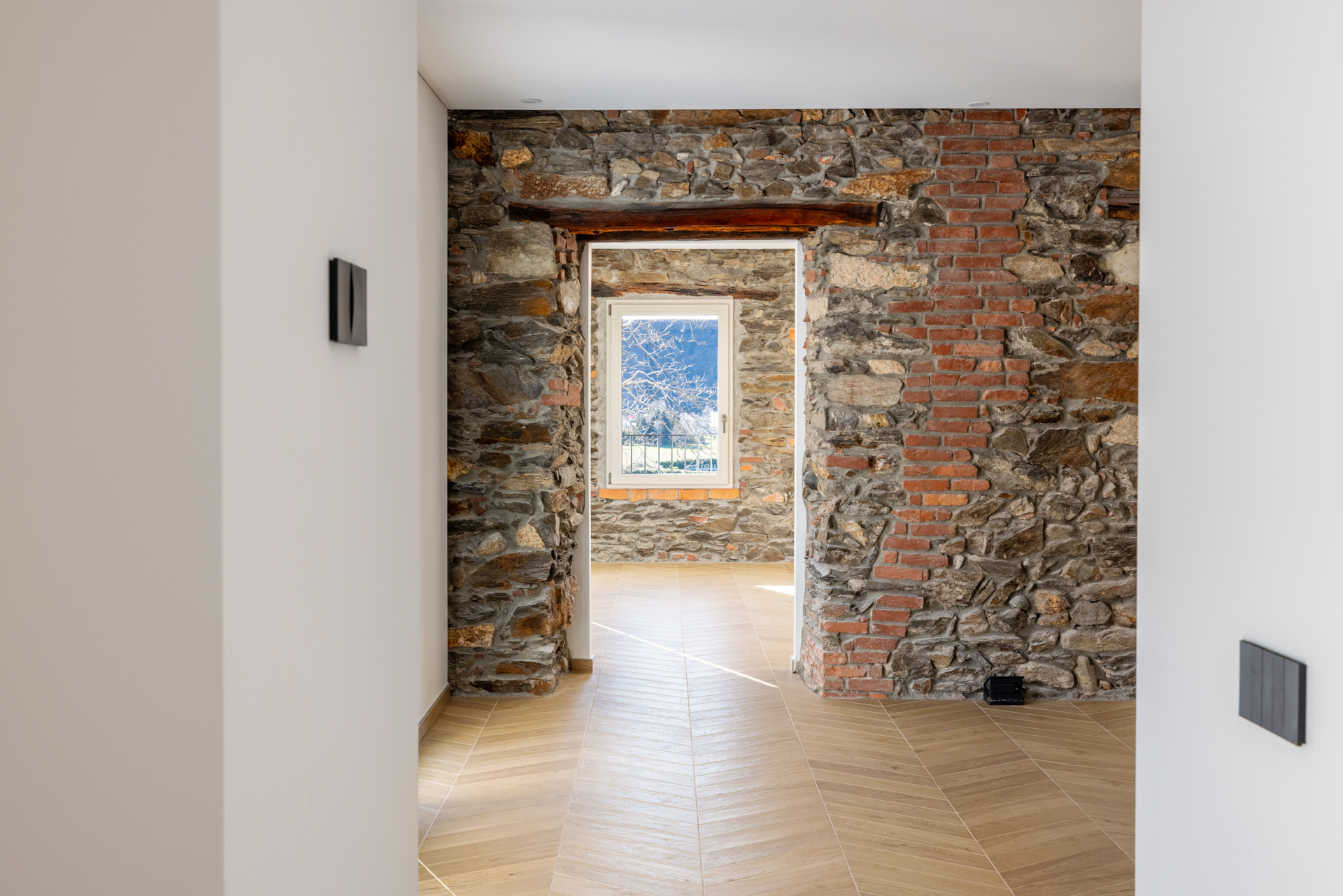 Interior view of a room with stone and brick walls, a window, and herringbone wood floors.
