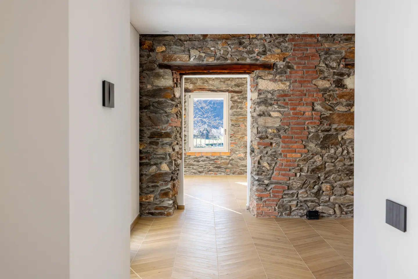 Interior view of a room with stone and brick walls, a window, and herringbone wood floors.