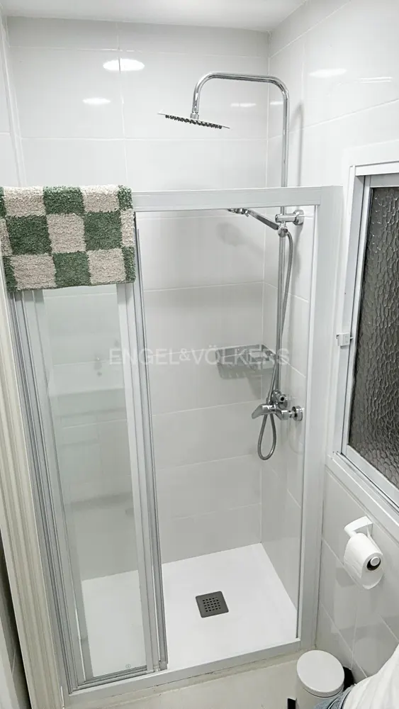 Modern walk-in shower with white tiled walls, a rainfall showerhead, and a green and white checkered bath mat.