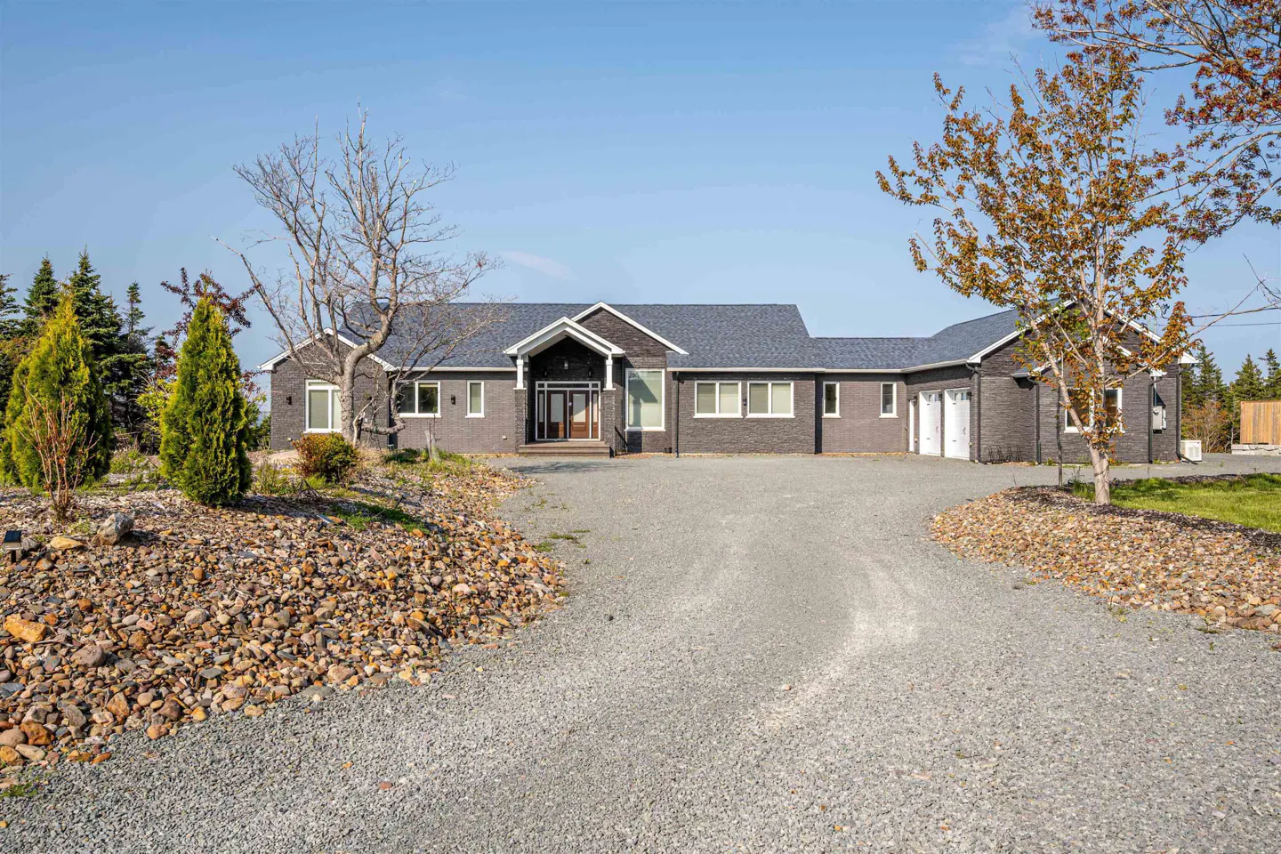 Single-story dark grey brick house with a gravel driveway, white trim, and a multi-car garage under a clear blue sky.
