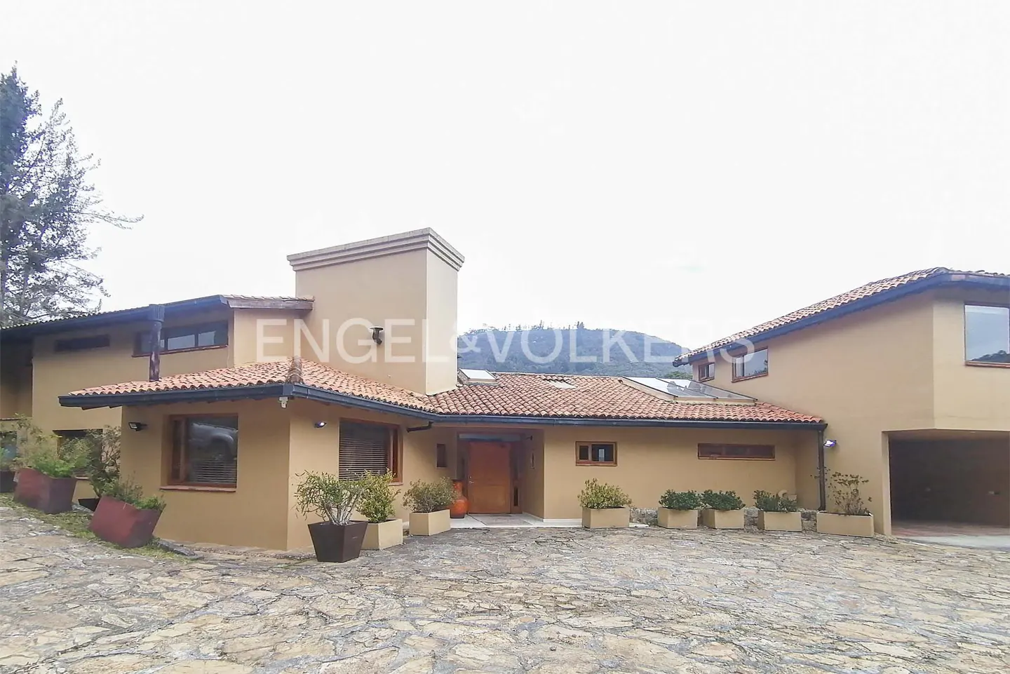 Tan stucco house with red tile roof and stone driveway. Engel & Volkers logo visible.