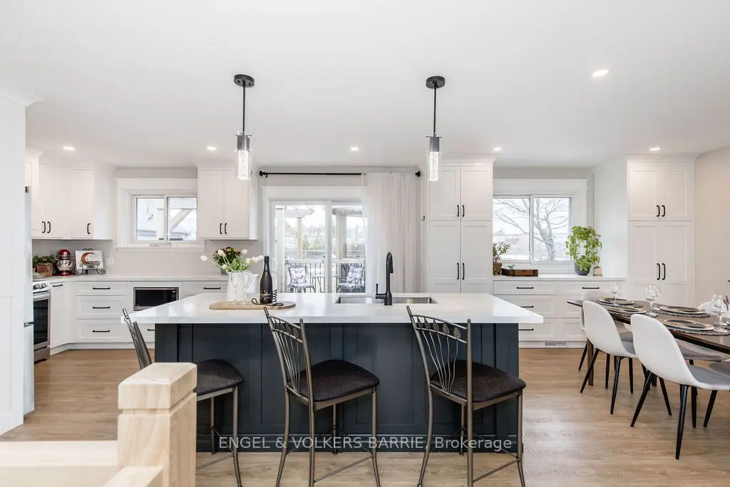 A bright, modern kitchen with white cabinets, a dark blue island with bar stools, and a dining table set for a meal.