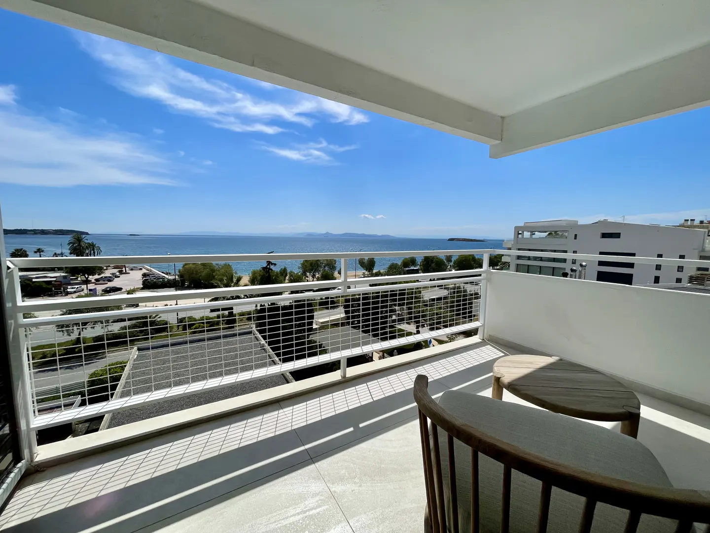Balcony view with a chair and table overlooking the ocean. White railings and a blue sky.