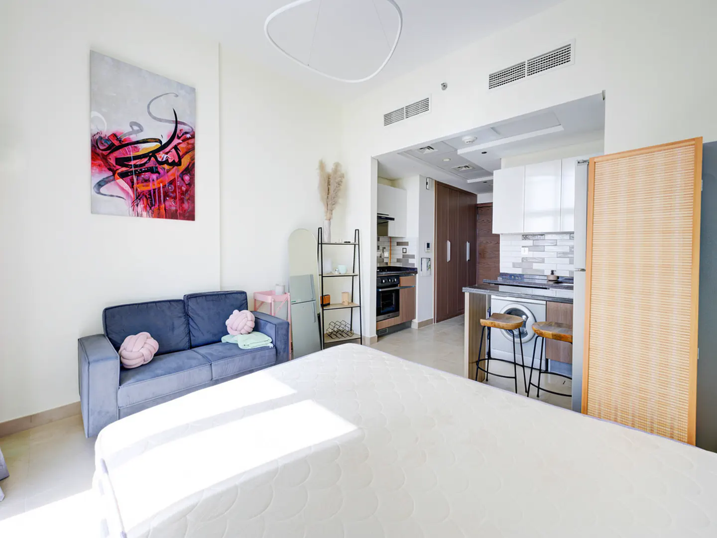 Bright studio apartment with a blue sofa, abstract art, and a kitchen with bar stools.