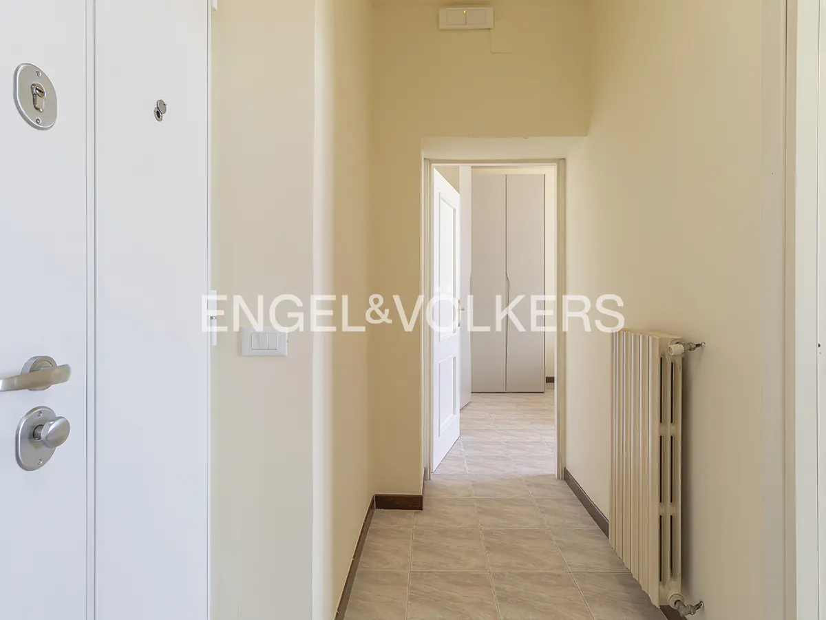 Entryway view with a white front door, tiled floor, radiator, and an open door leading to a room with a white wardrobe.