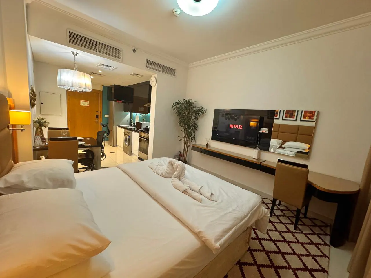 A studio apartment with a bed, kitchen, and TV with Netflix on the screen. The bed has white sheets and a swan towel.