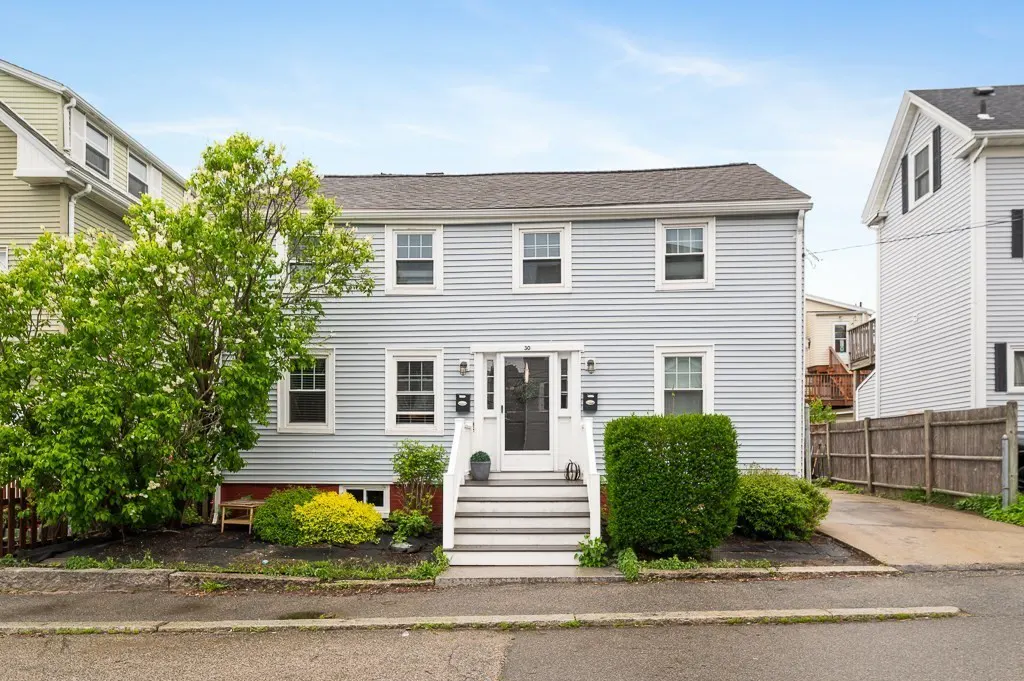 Two-story light blue house with white trim, a black front door, and a gray roof on a sunny day.