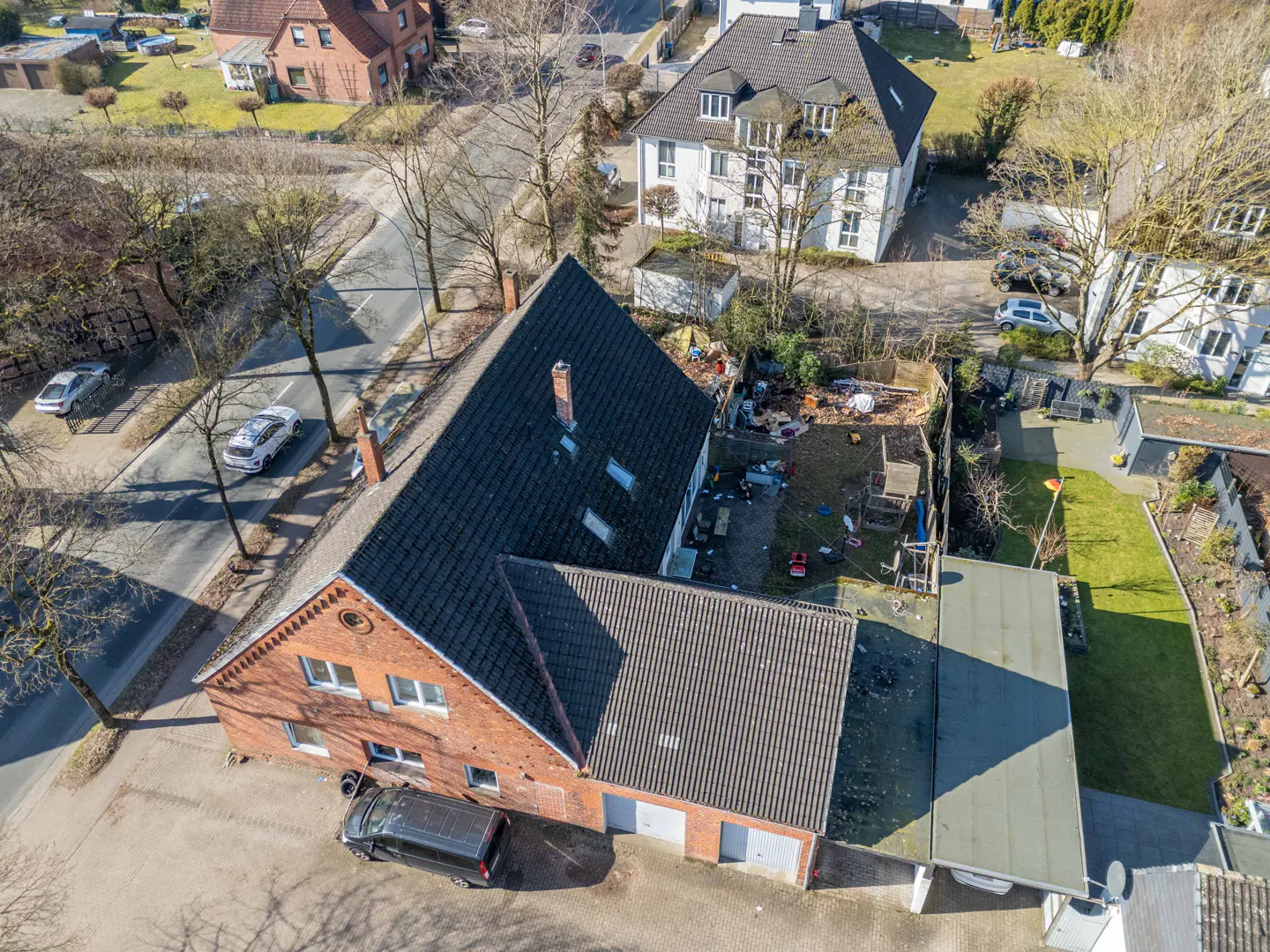 Aerial view of a red brick house with a dark gray roof, a black car parked in front, and a messy backyard.