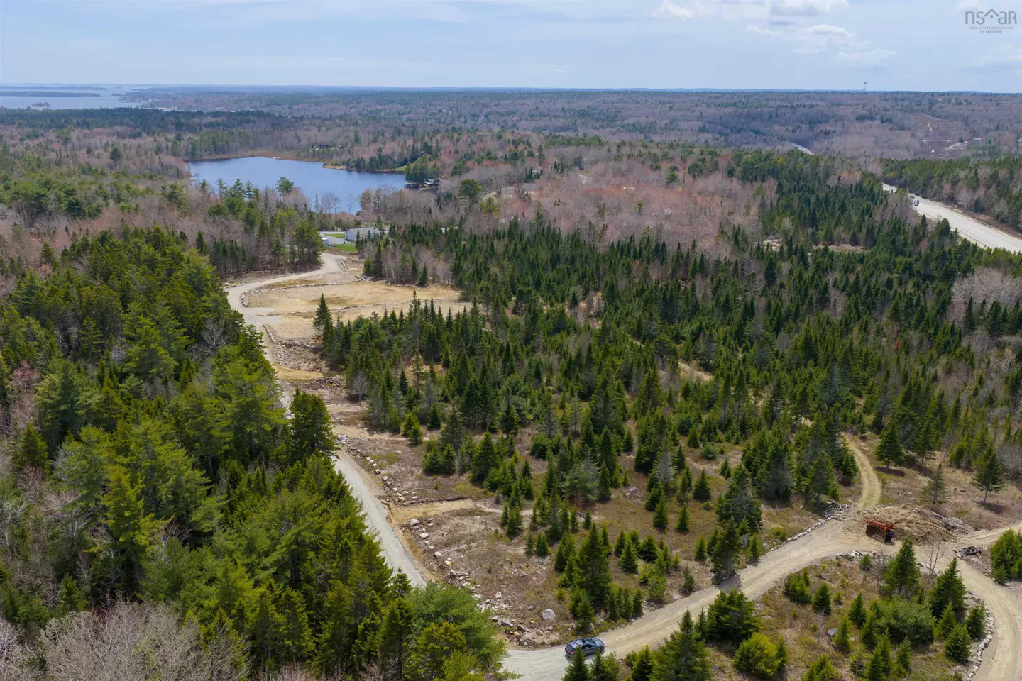 Aerial view of a wooded property with a lake in the background. A dirt road winds through the trees.