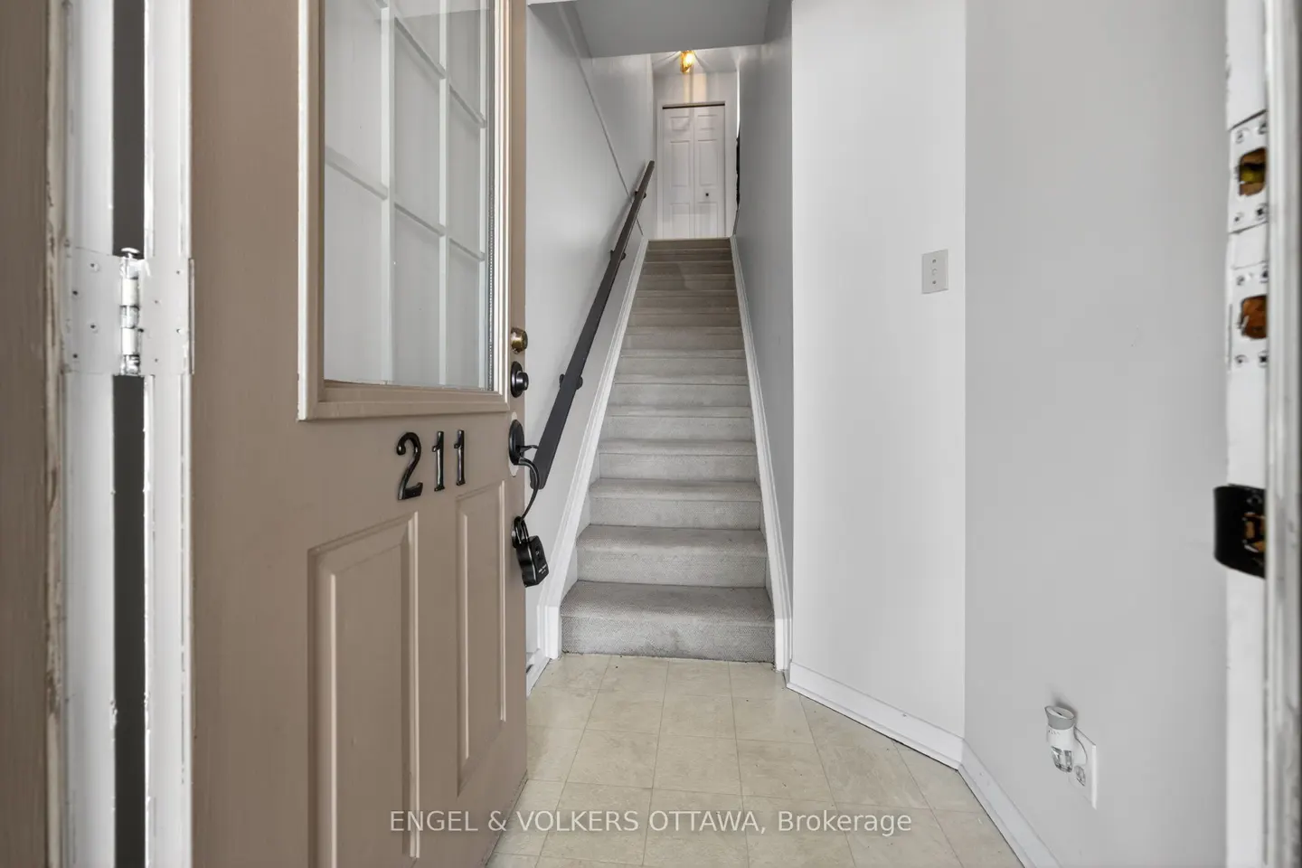 Open door with "211" leads to a staircase. The walls are white, and the stairs are carpeted in gray. A black handrail is visible.