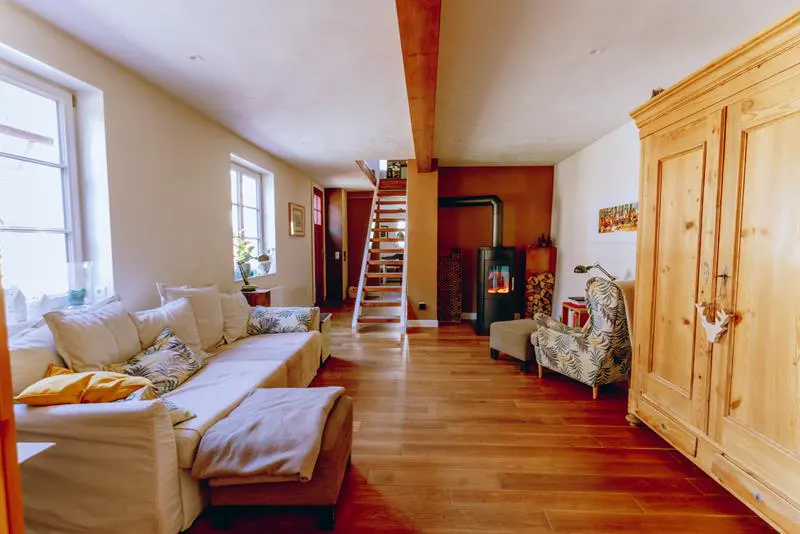 Living room with wood floors, white sofa, wood burning stove, and wooden staircase.