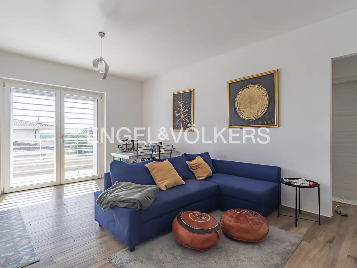 Bright living room with blue sectional sofa, tan pillows, and two brown ottomans on a gray rug. Art on the white walls.