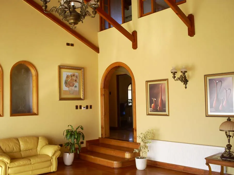 Interior view of a home with yellow walls, wood floors, and a high ceiling with exposed beams. A yellow sofa and framed artwork decorate the space.