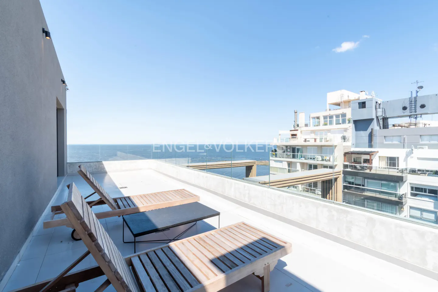 Balcony with ocean view, featuring lounge chairs, a glass railing, and Engel & Volkers logo.