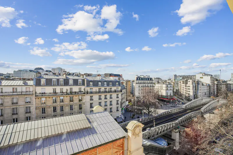 Paris cityscape view with buildings, a metal bridge, and a blue sky with white clouds.