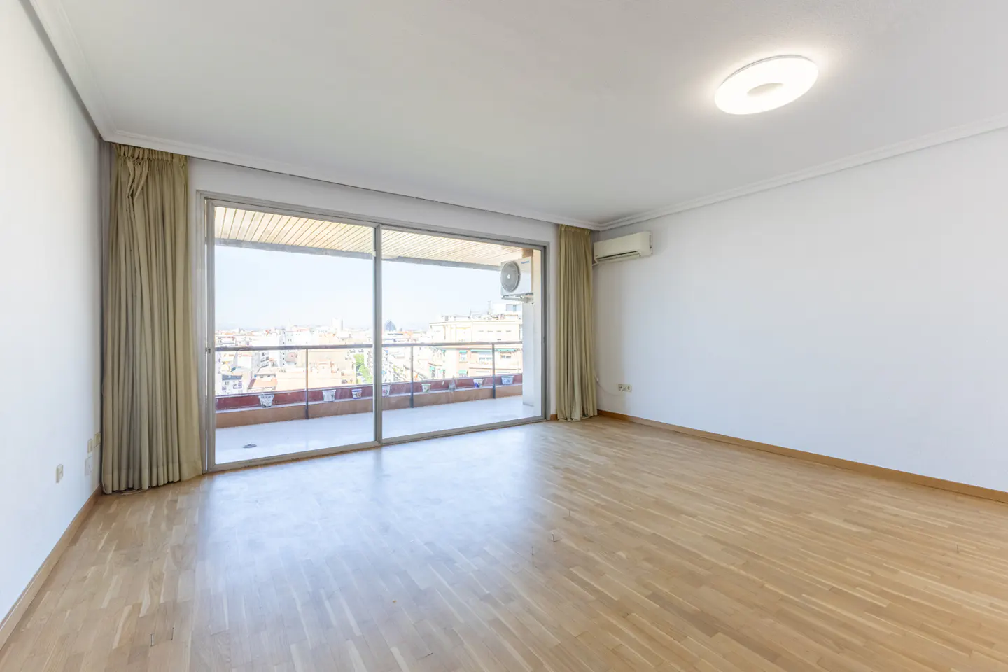 Bright, empty room with wood floors, white walls, and large sliding glass doors to a balcony with a city view.
