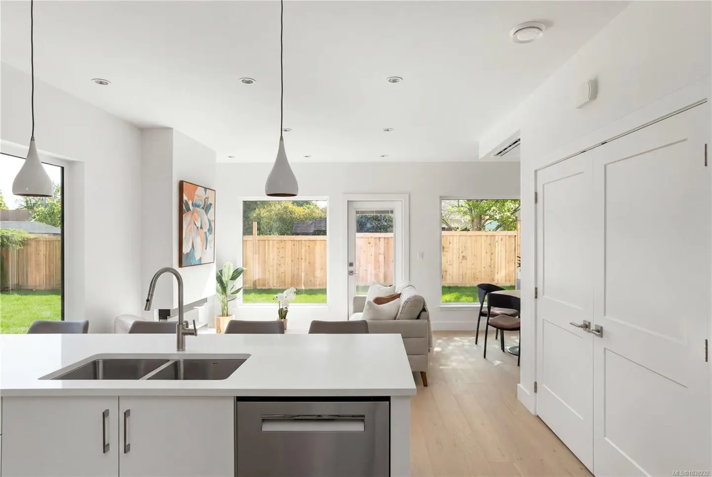 Bright, modern kitchen with white cabinets, stainless steel appliances, and a large island. Windows overlook a fenced backyard with green grass.
