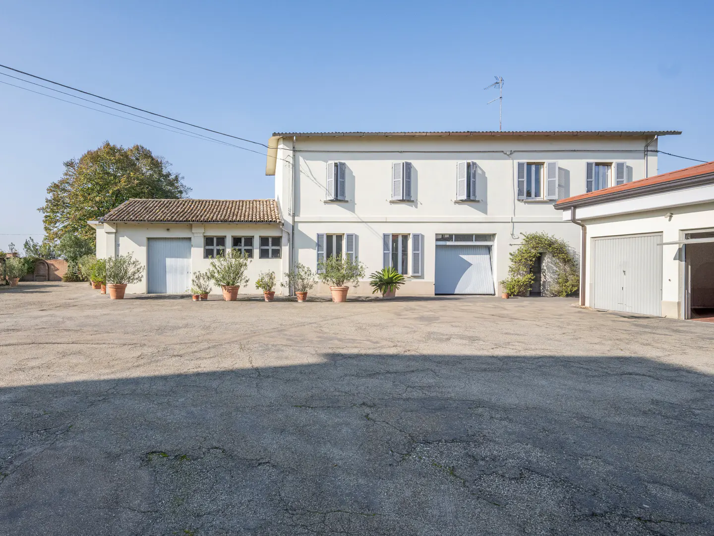 Two-story white house with gray shutters and garage doors, potted plants, and a large paved driveway.