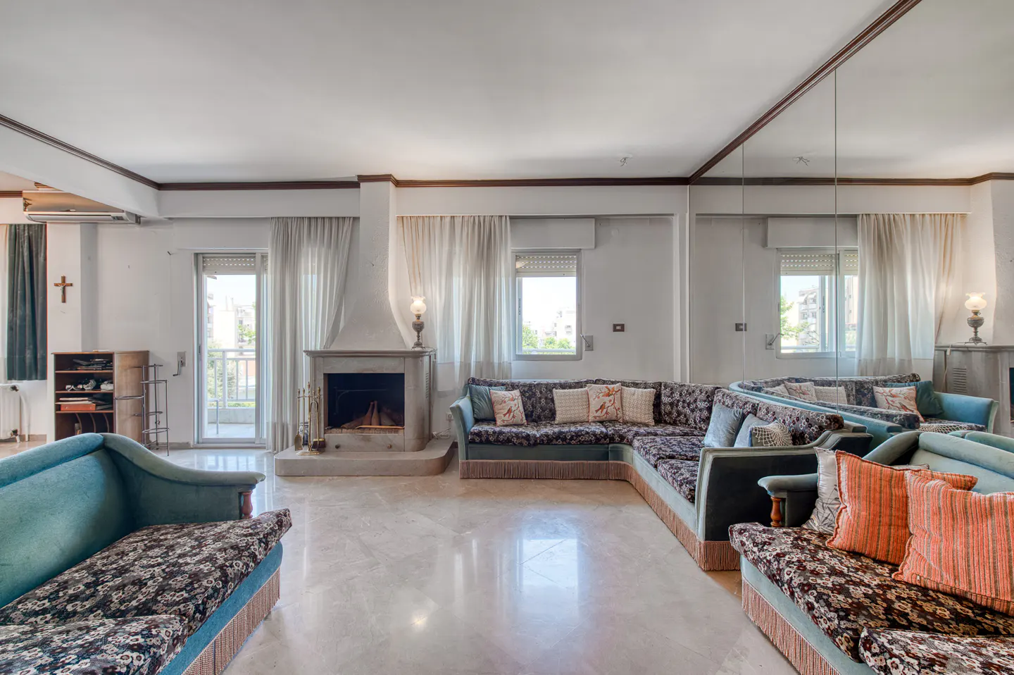 Spacious living room with marble floors, a stone fireplace, patterned sofas, and a large mirrored wall.