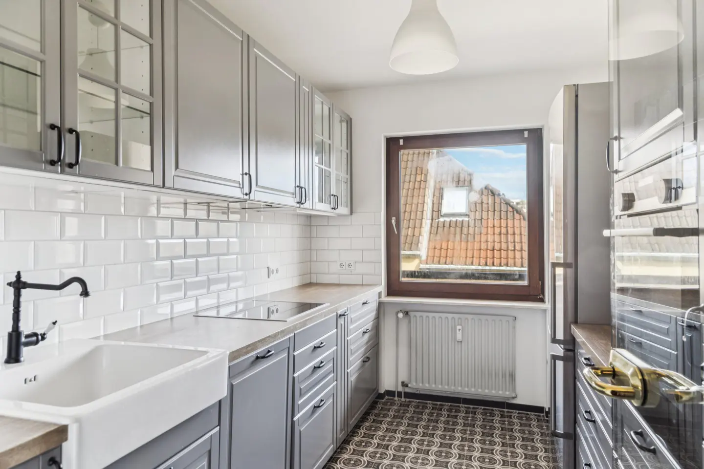 Bright kitchen with gray cabinets, white subway tile, and a farmhouse sink. A window overlooks rooftops.