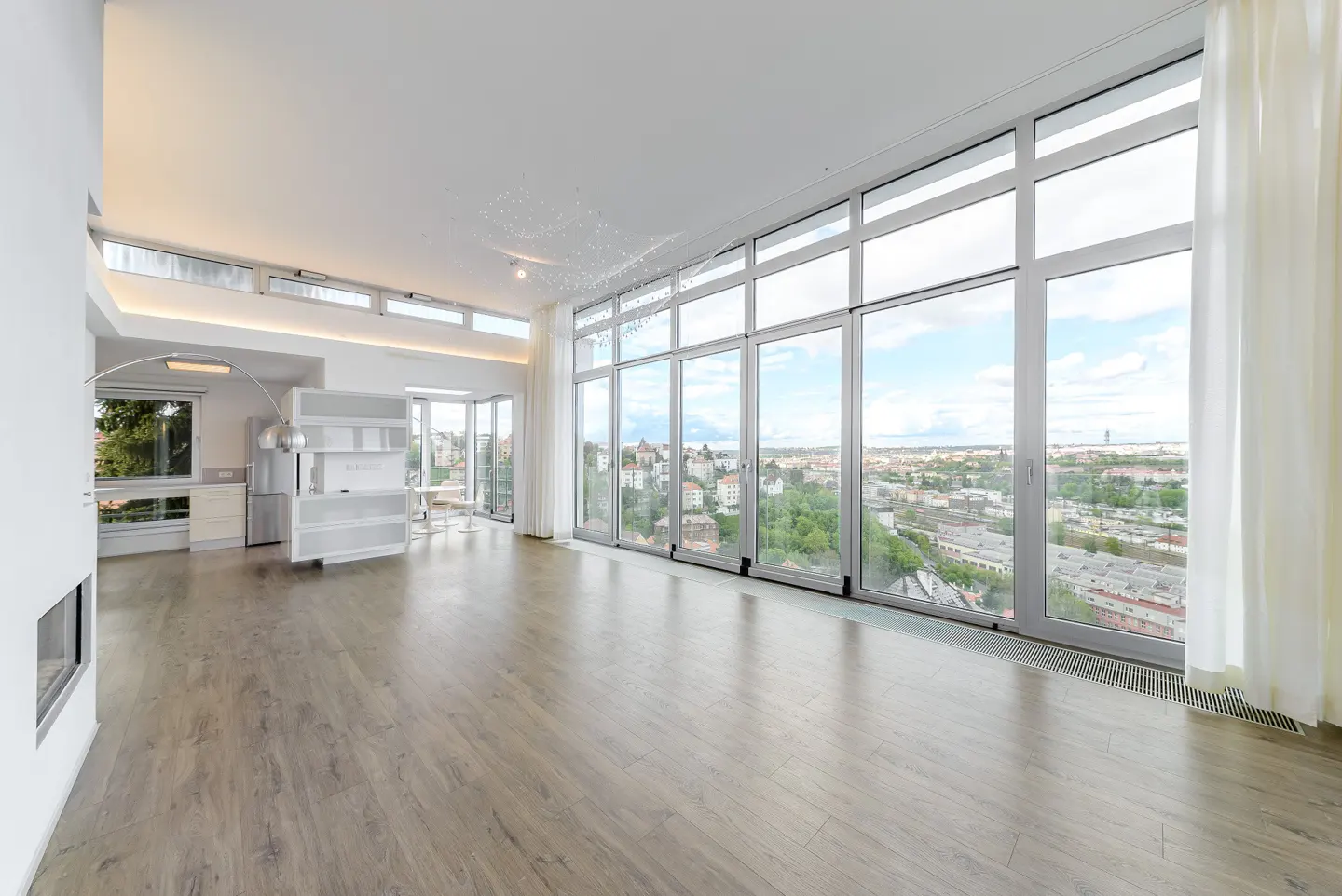 Spacious, modern living room with light wood floors, high ceilings, and a wall of windows overlooking a city landscape.