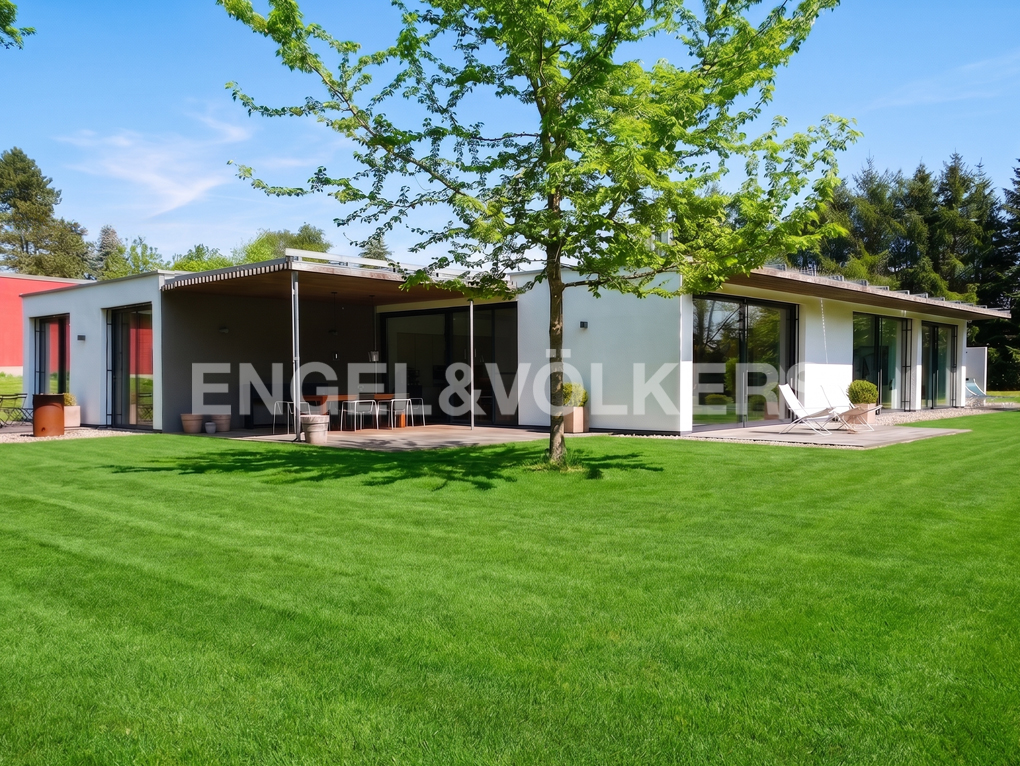 Modern white single-story home with a large covered patio, expansive green lawn, and a large tree under a clear blue sky. [AI-generated text]