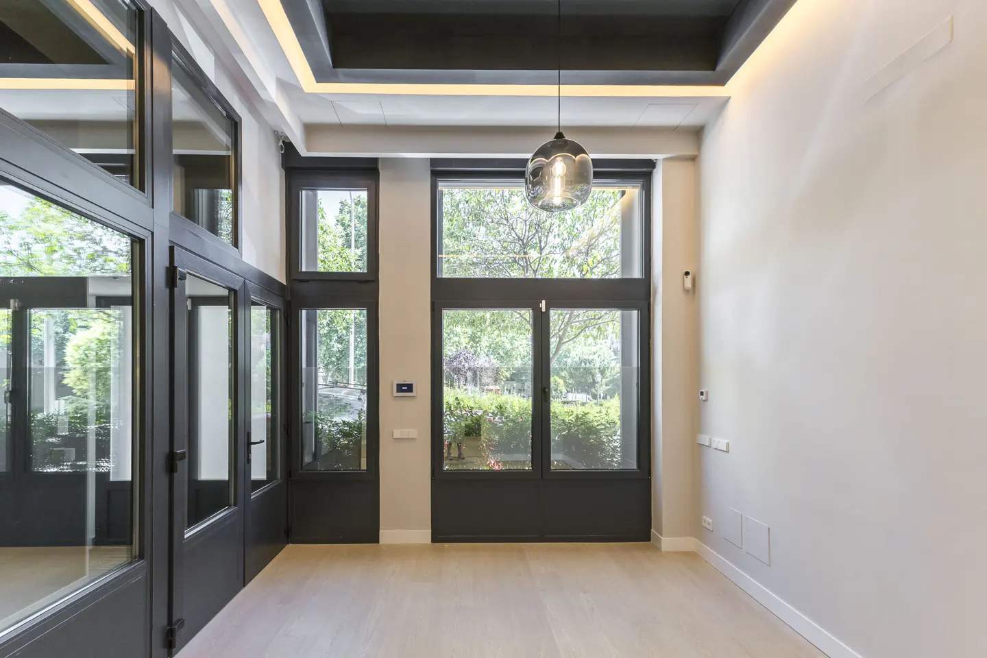 Modern room with light wood floors, high ceilings, dark-framed windows, and a hanging glass pendant light.