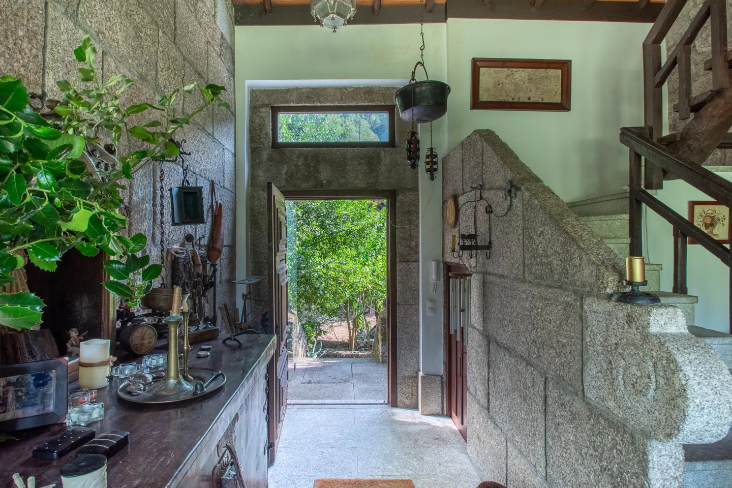 Rustic stone entryway with a wooden console table, hanging decor, and an open door revealing a lush green garden.