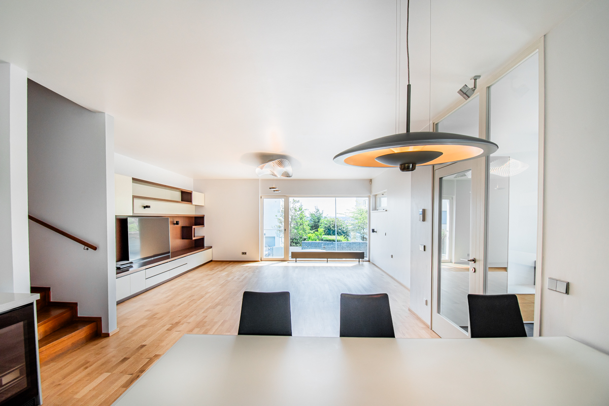 Modern living room with hardwood floors, a sleek media wall, a large pendant light, and a view of a patio through glass.
