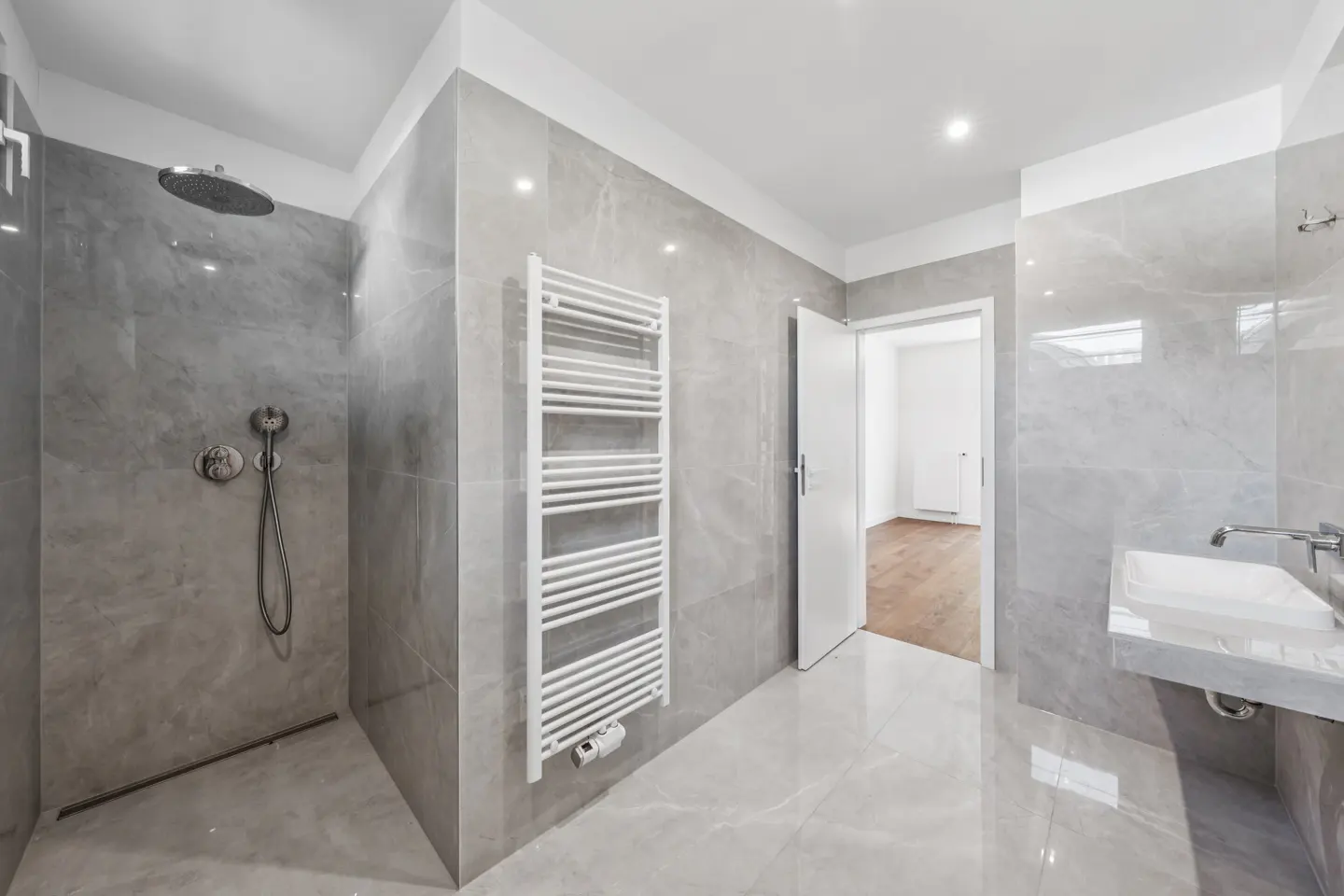 Bright bathroom with gray marble tile, white sink, towel rack, and open door to a room with wood floors.