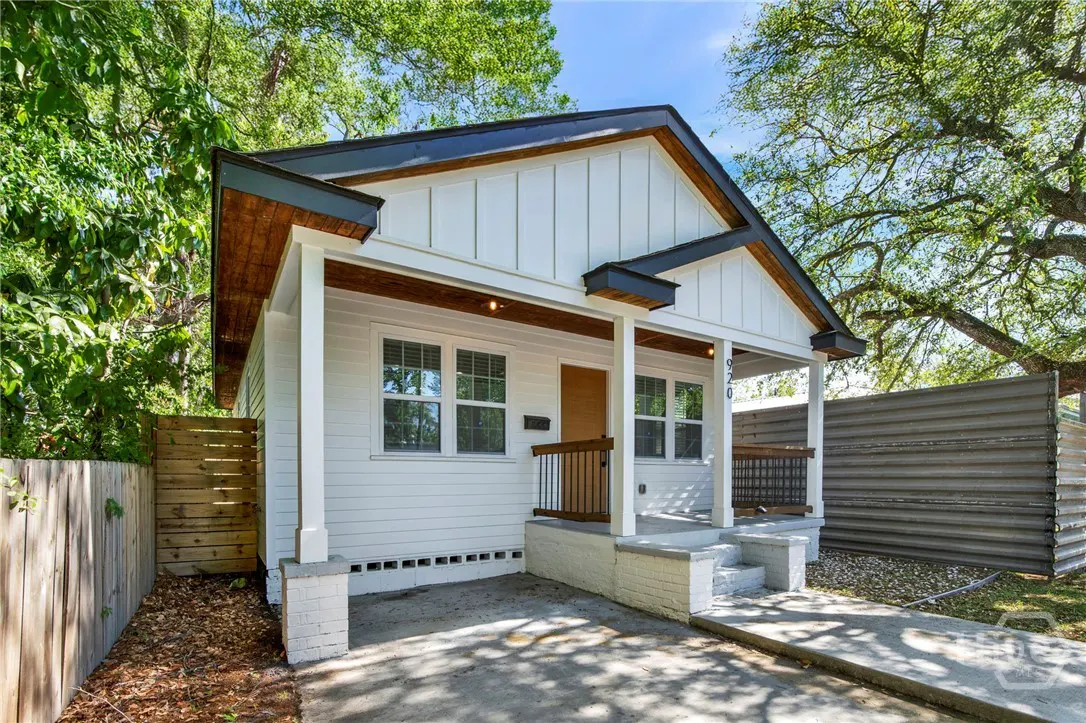 Exterior view of a white, single-story house with a dark roof and a small front porch. The house has a modern design with vertical siding.