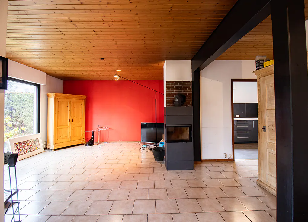 A spacious living room with a red accent wall, a wood-paneled ceiling, and a modern fireplace.