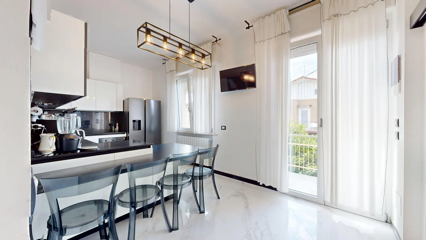 Modern kitchen with white cabinets, black countertops, four transparent chairs, and a balcony door with white curtains.