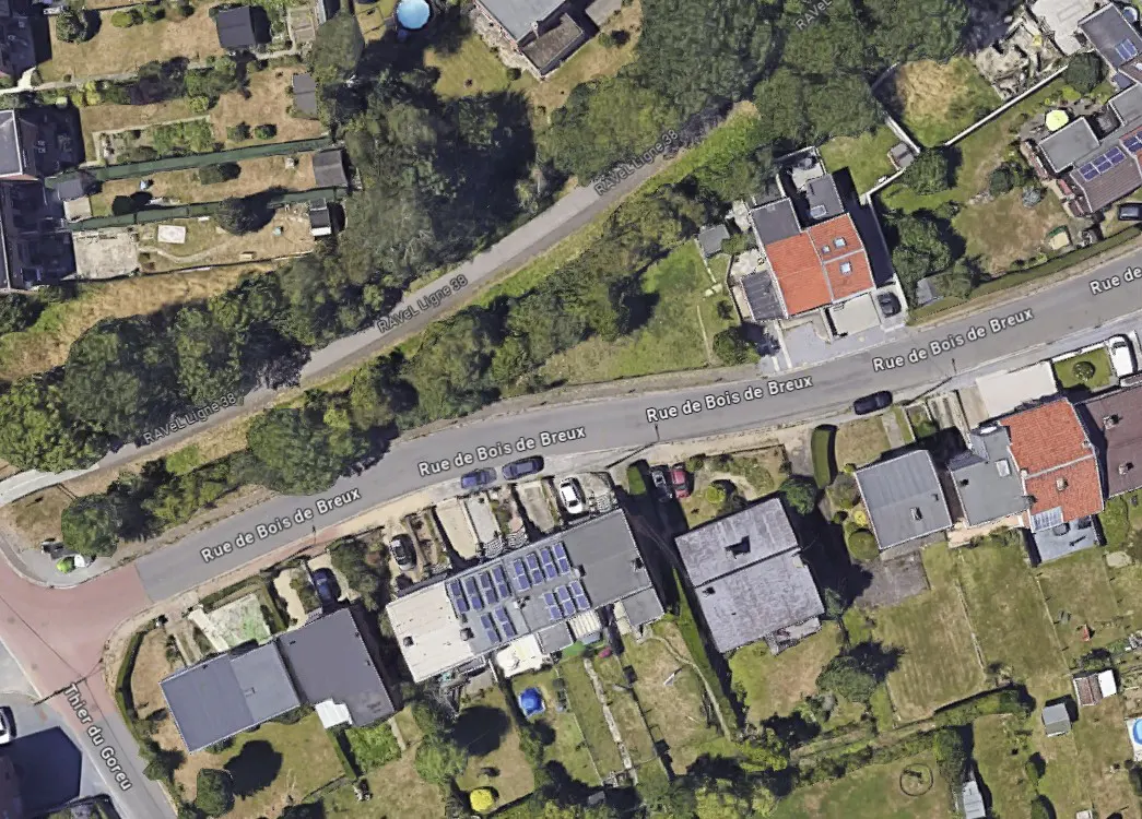 Aerial view of a residential area with houses, roads, and green spaces. Solar panels are visible on one roof.