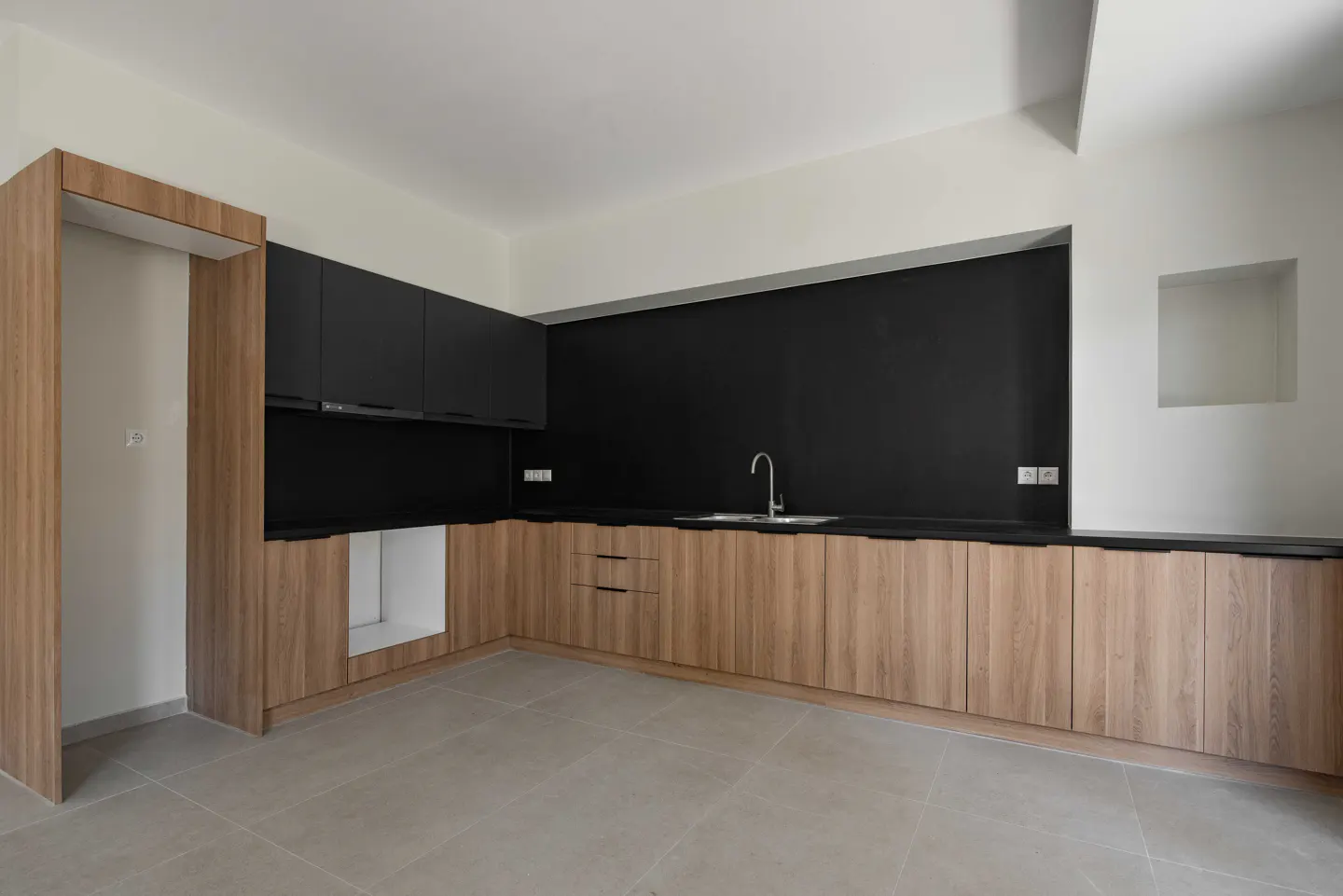 A modern kitchen with light wood cabinets, black countertops and backsplash, and a stainless steel sink.
