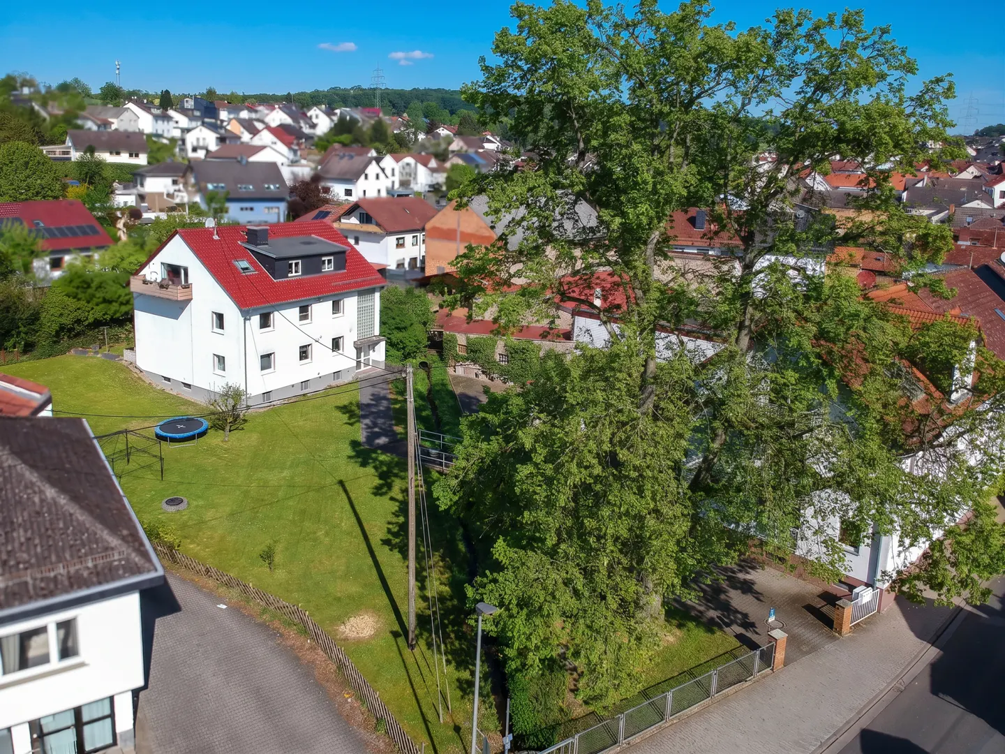 Aerial view of a white house with a red roof, surrounded by green lawn and trees in a residential neighborhood.