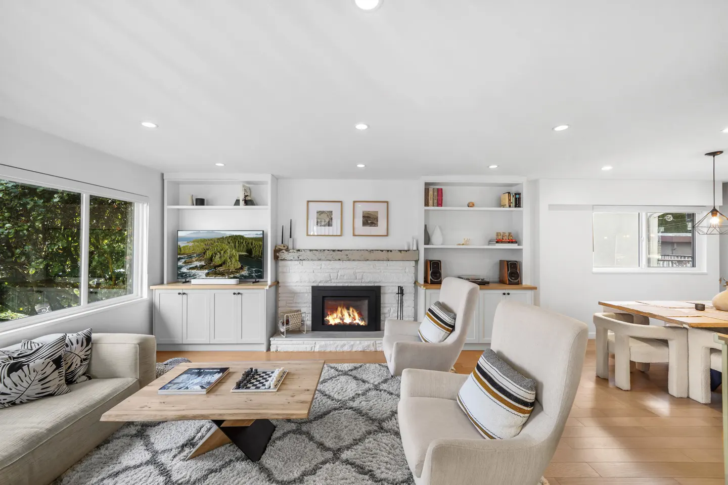 Bright living room with a white fireplace, built-in shelves, a sofa, and two armchairs. A wooden coffee table sits on a gray patterned rug.