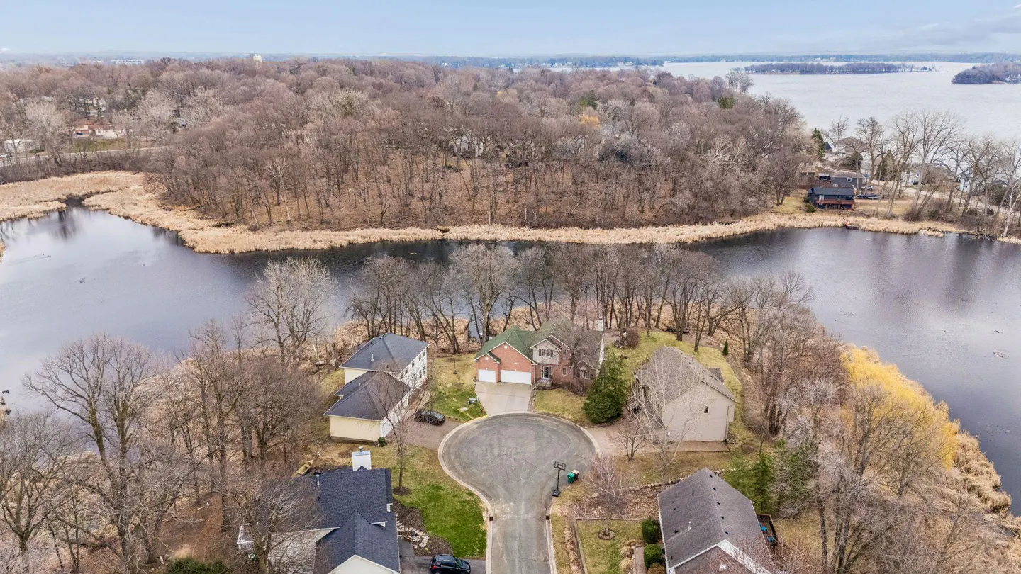 Aerial view of homes on a peninsula surrounded by water and trees under a cloudy sky.