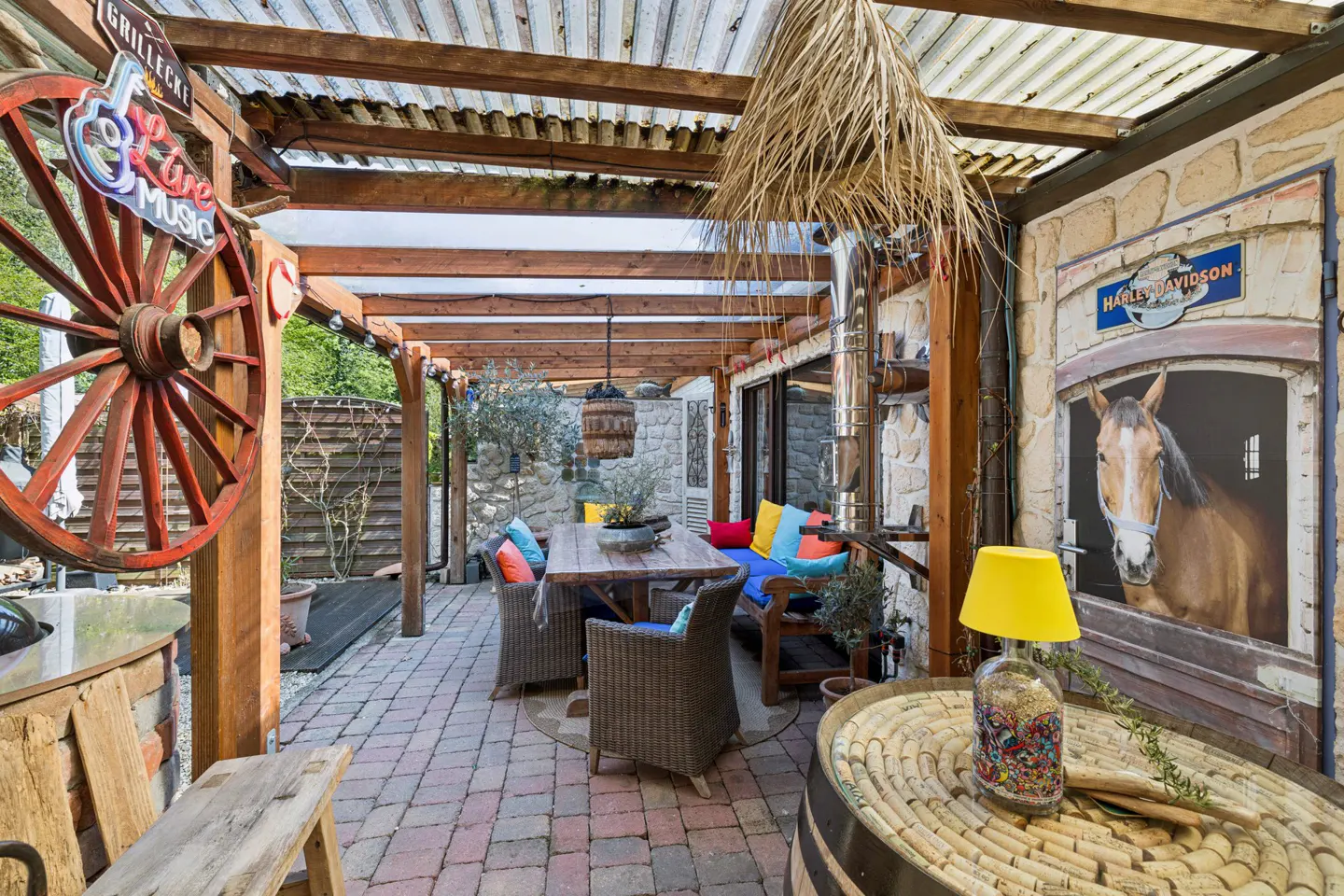 Outdoor patio with brick flooring, wooden pergola, dining table, and horse mural. A large red wheel and "Live Music" sign decorate the space.