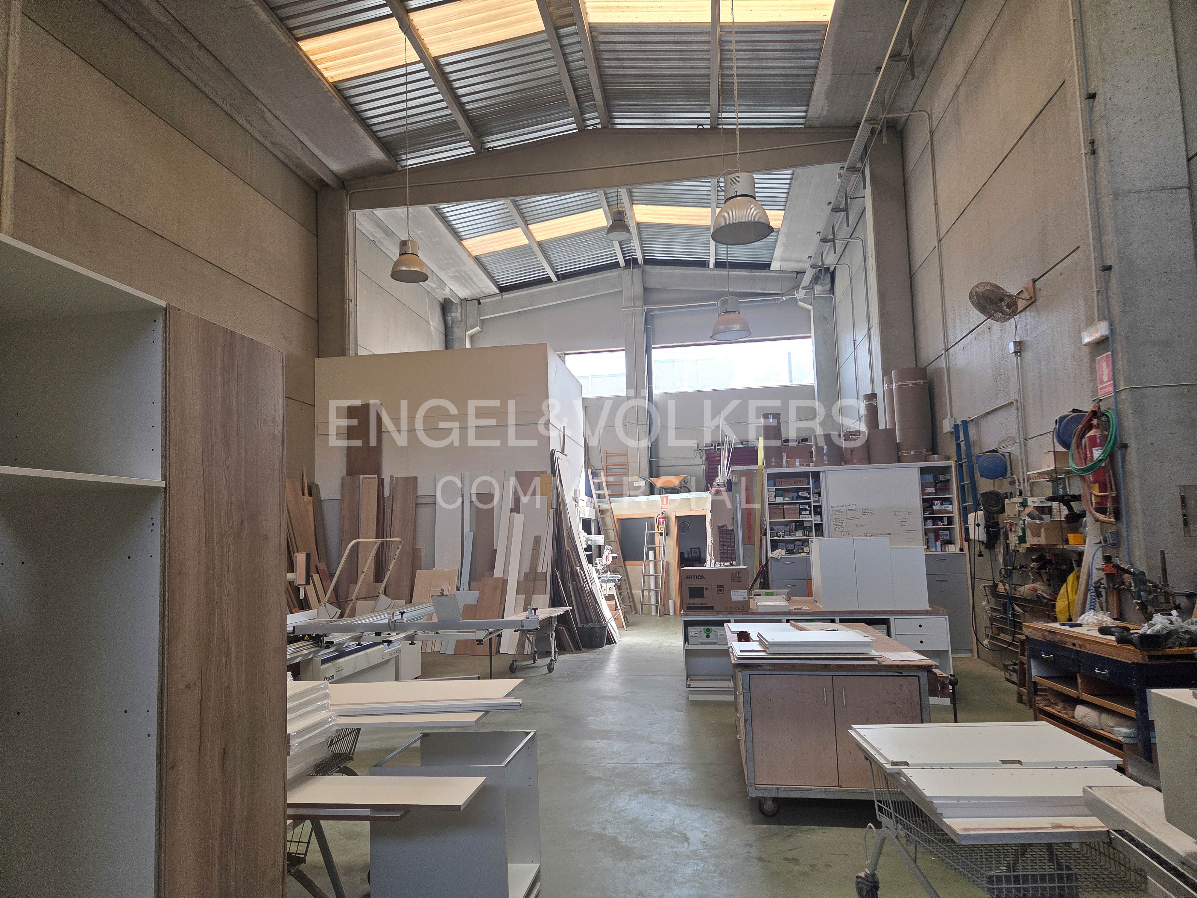 A bright, spacious workshop with wood materials, tools, and equipment. The Engel & Volkers logo is visible in the background.