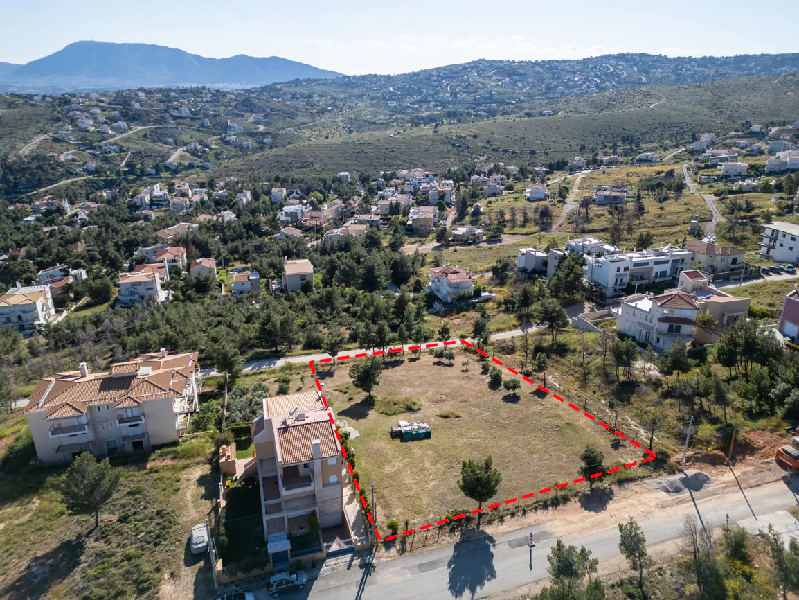 Aerial view of a vacant lot outlined in red, surrounded by trees, houses, and mountains in the background.