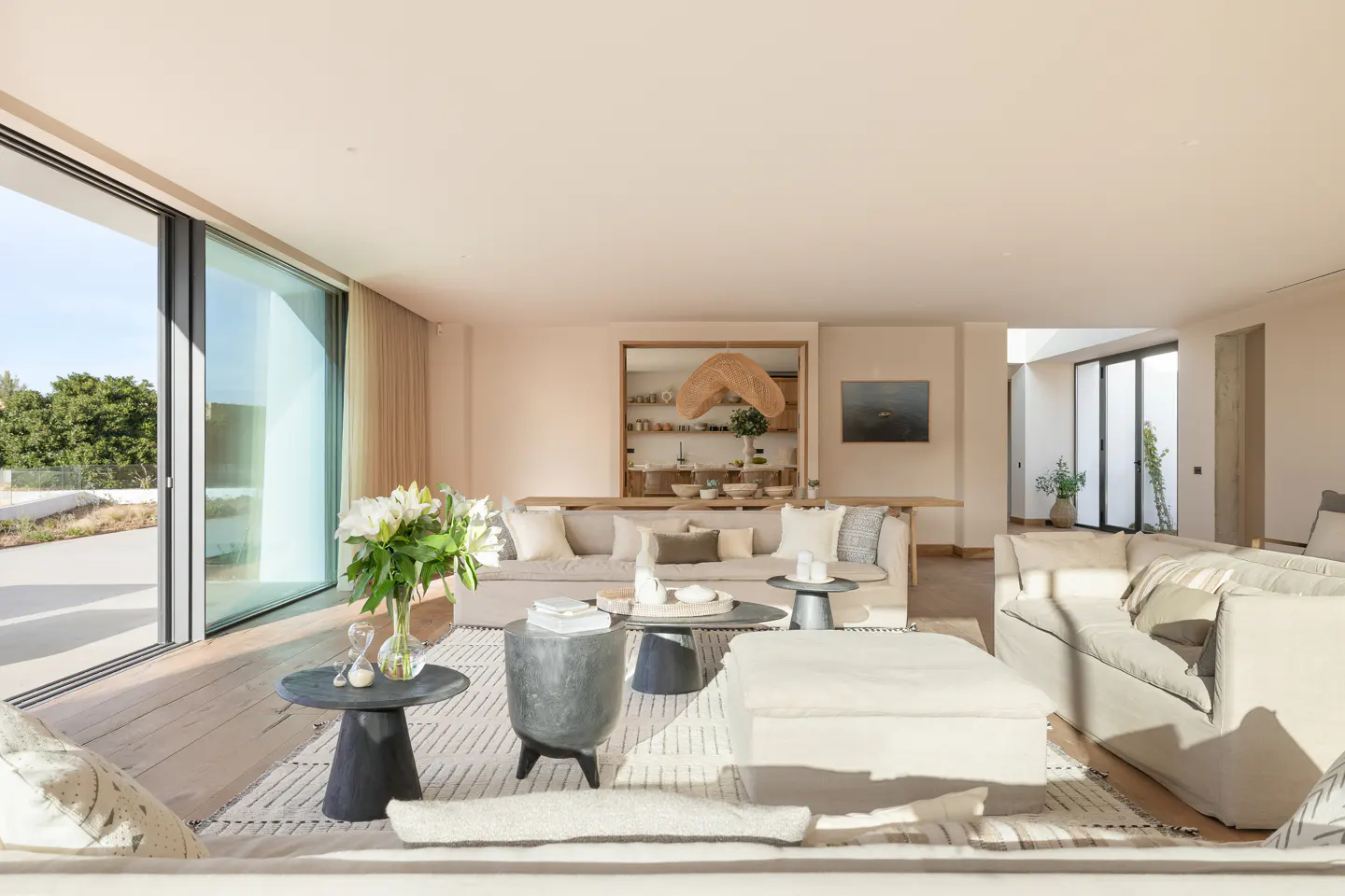 Bright, open living room with beige sofas, wooden floors, and large sliding glass doors to the outside. Neutral tones and natural light.