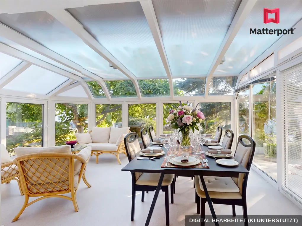 Bright sunroom with a glass ceiling, a black dining table set for eight, and wicker furniture. A large floral arrangement sits in the center of the table.