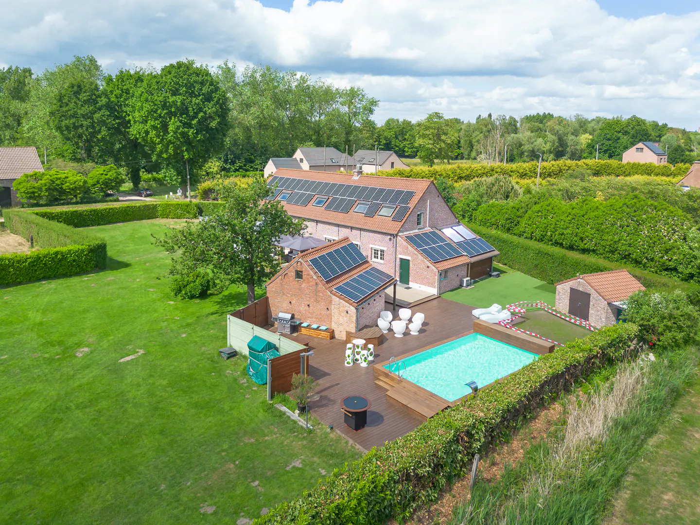 Aerial view of a brick house with solar panels, a pool, and a green lawn.