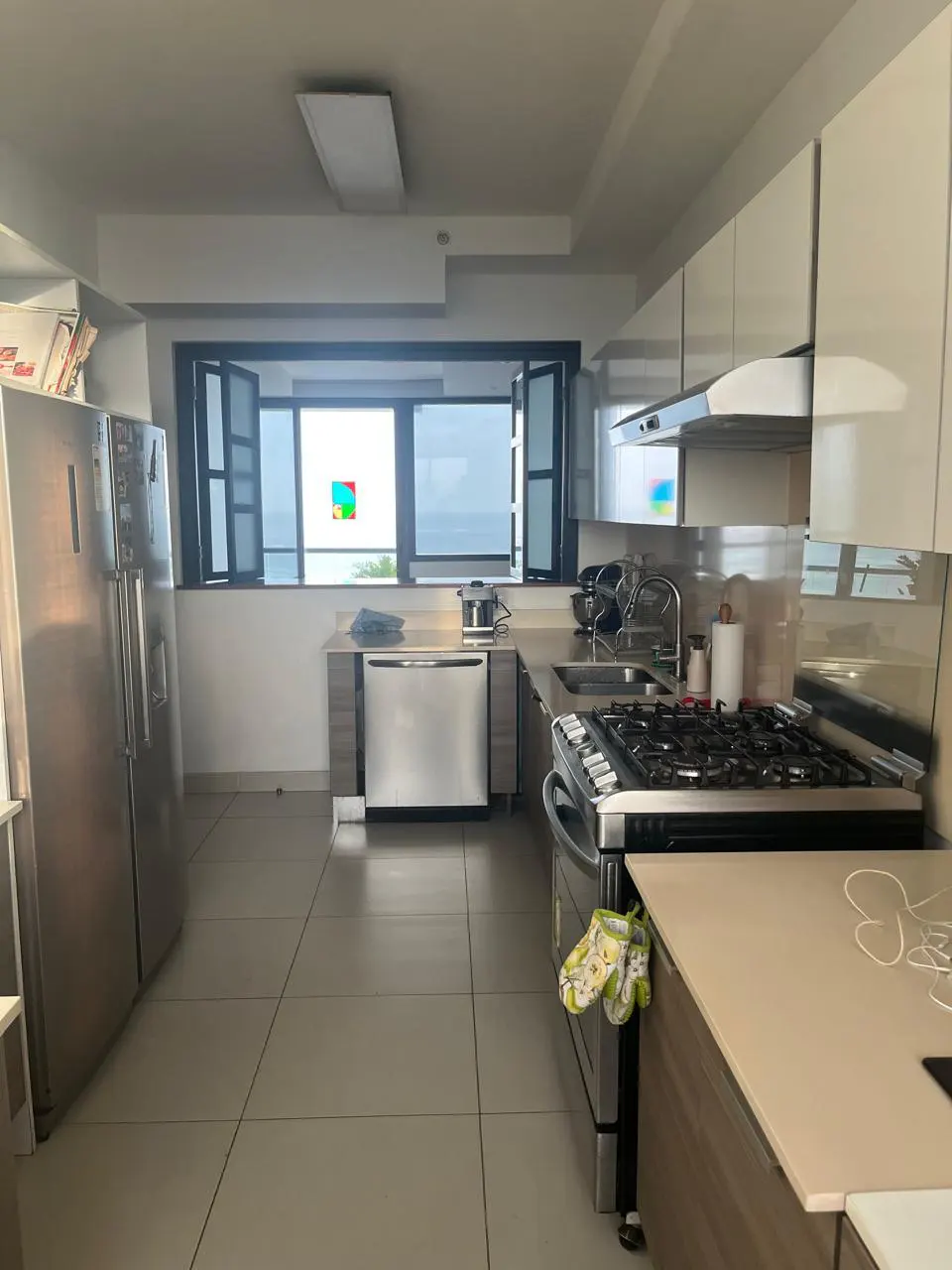 A modern kitchen with stainless steel appliances, white cabinets, and a large window overlooking the ocean.
