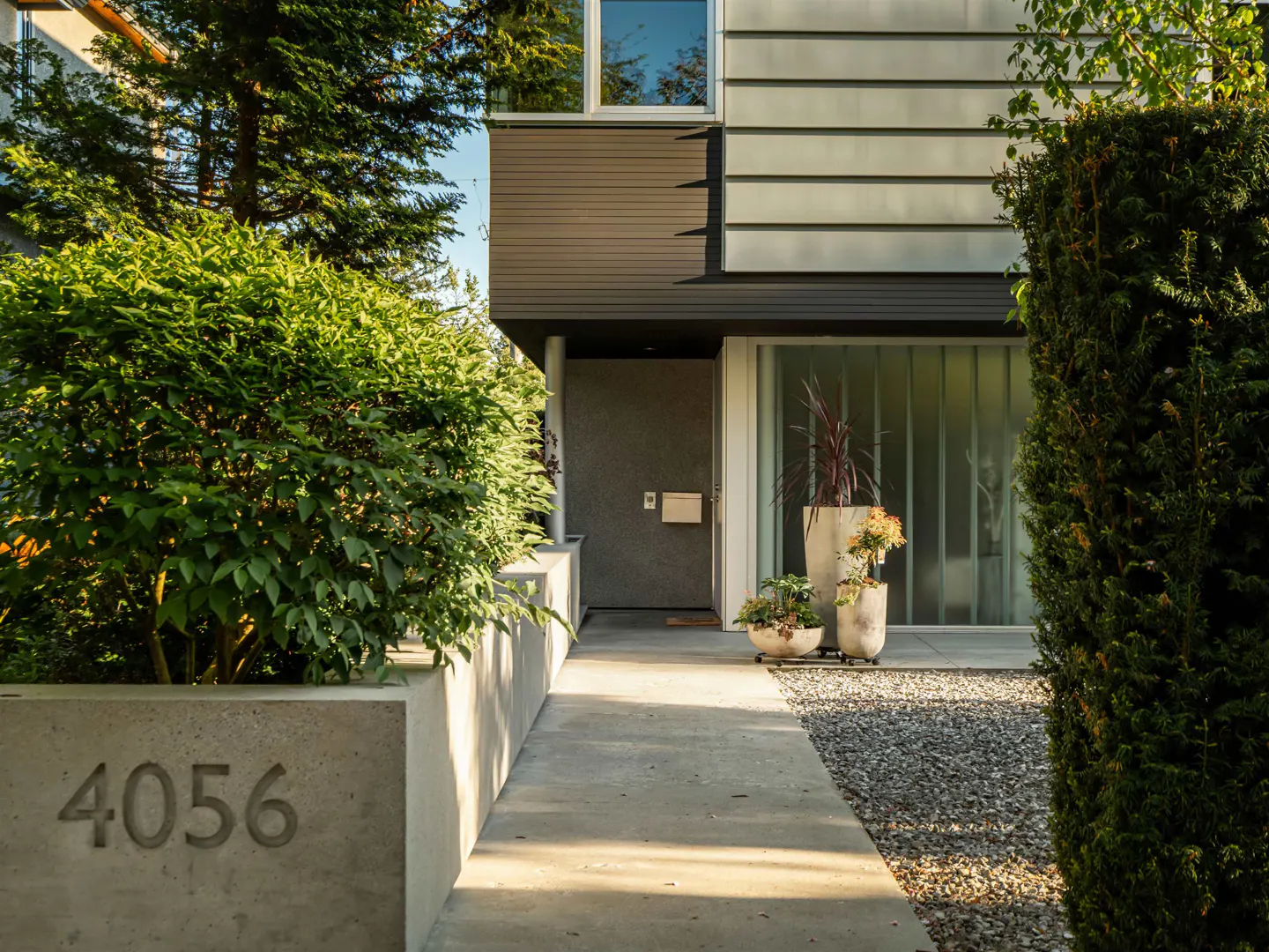Modern home exterior with a concrete walkway leading to a gray front door. Planters and greenery add curb appeal. Address "4056" is visible.