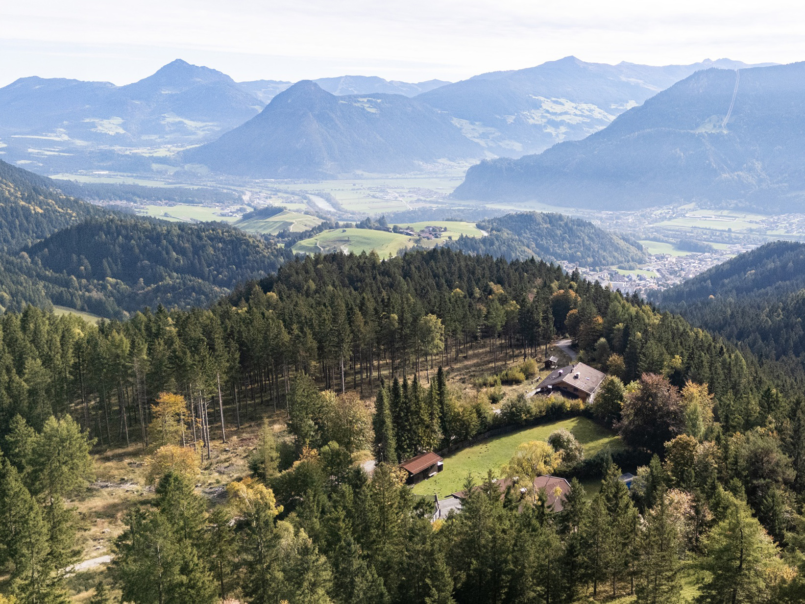 Aerial view of a house nestled in a lush green forest with a scenic mountain valley landscape in the background. [AI-generated text]