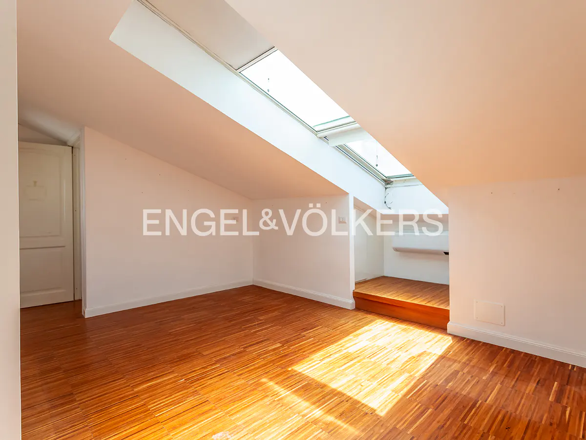 Attic room with wood floors, white walls, and skylights. Engel & Völkers logo on the wall.